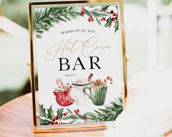 Può includere: Un cartello con cornice dorata, sfondo bianco e illustrazioni ad acquerello verde e rosso di agrifoglio e bacche. Il cartello recita "Warm up at the Hot Cocoa Bar Enjoy!" con tre illustrazioni di tazze di cioccolata calda.