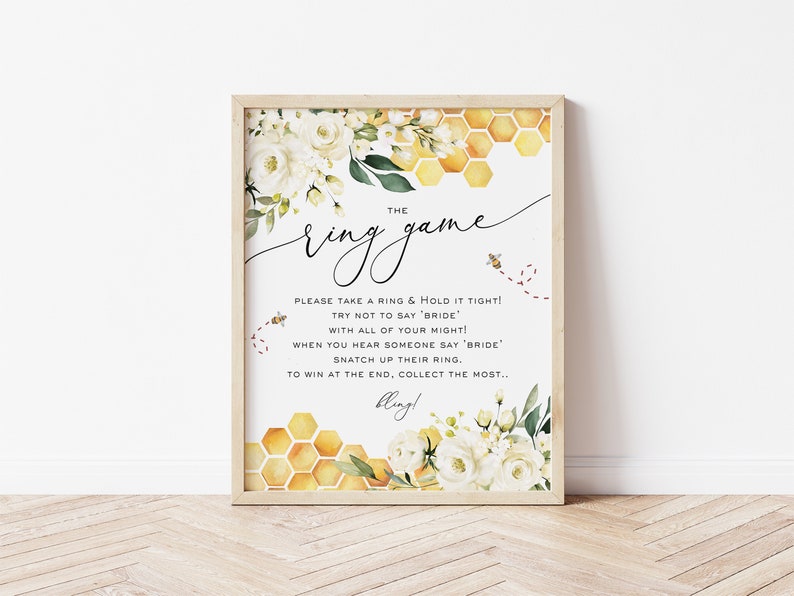 May include: A printable bridal shower game card with a white background and a honeycomb pattern. The text reads "The Ring Game" and includes instructions for the game. The card is decorated with white flowers and green leaves.