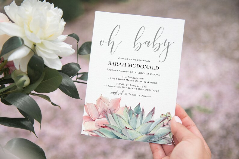 May include: Baby shower invitation with the words "oh baby" in elegant script. The invitation includes details for Sarah McDonald's baby shower, with a watercolor succulent design at the bottom. The invitation is held by a person.