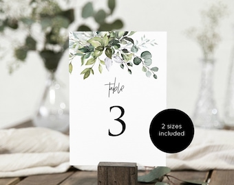 May include: A white table number card with a watercolor illustration of green leaves and the text "Table 3" in black.