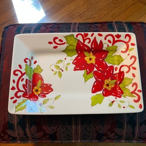May include: Rectangular white ceramic serving platter with a festive poinsettia design. The platter features large red poinsettia flowers with green leaves and red swirls. The flowers have yellow centers and red berries.