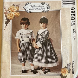 May include: A sewing pattern for children's clothing from McCall's. The pattern is for a girl's dress and a boy's outfit. The dress is a gingham check with a white lace trim. The boy's outfit is a gingham check shirt with a white collar and a pair of gingham check pants. The pattern is called "Ruffles and Lace Treasured Collection" and the pattern number is 6858.