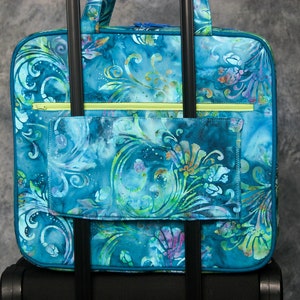 May include: A blue and green patterned travel bag with a zippered pocket and two handles. The bag is attached to a rolling luggage set.