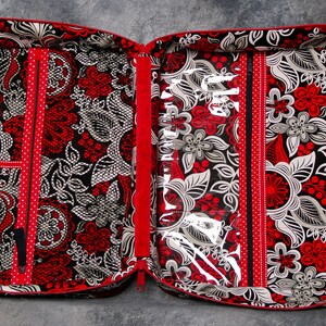 May include: A red and black zippered travel case with multiple compartments and a clear plastic window. The case has a floral pattern and is lined with red fabric.