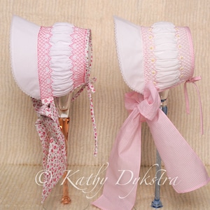 May include: Two white bonnets with pink trim and bows. One bonnet has a pink floral print bow and the other has a pink gingham bow.