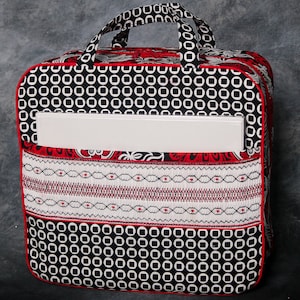 May include: Black and white fabric tote bag with red trim and a white pocket. The bag has a geometric pattern of circles and a white pocket with a red trim.