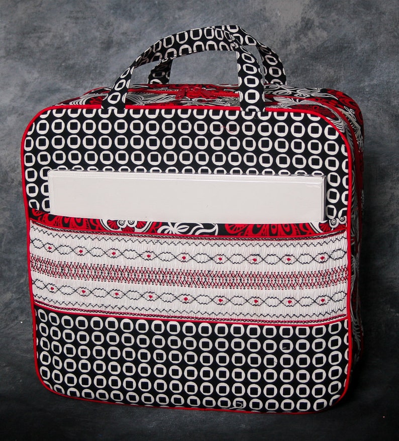 May include: Black and white fabric tote bag with red trim and a white pocket. The bag has a geometric pattern of circles and a white pocket with a red trim.