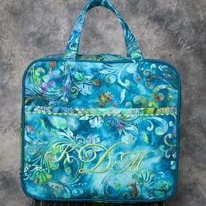 May include: A teal blue tote bag with a green floral pattern and a green embroidered monogram "KDM".