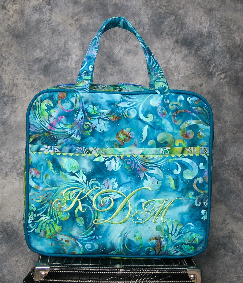 May include: A teal blue tote bag with a green floral pattern and a green embroidered monogram "KDM".