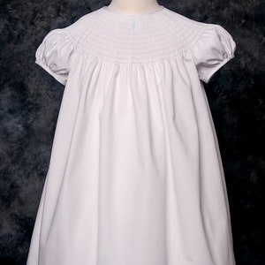 May include: A white smocked dress with short puffed sleeves. The dress is made of a soft, lightweight fabric and has a simple, elegant design.