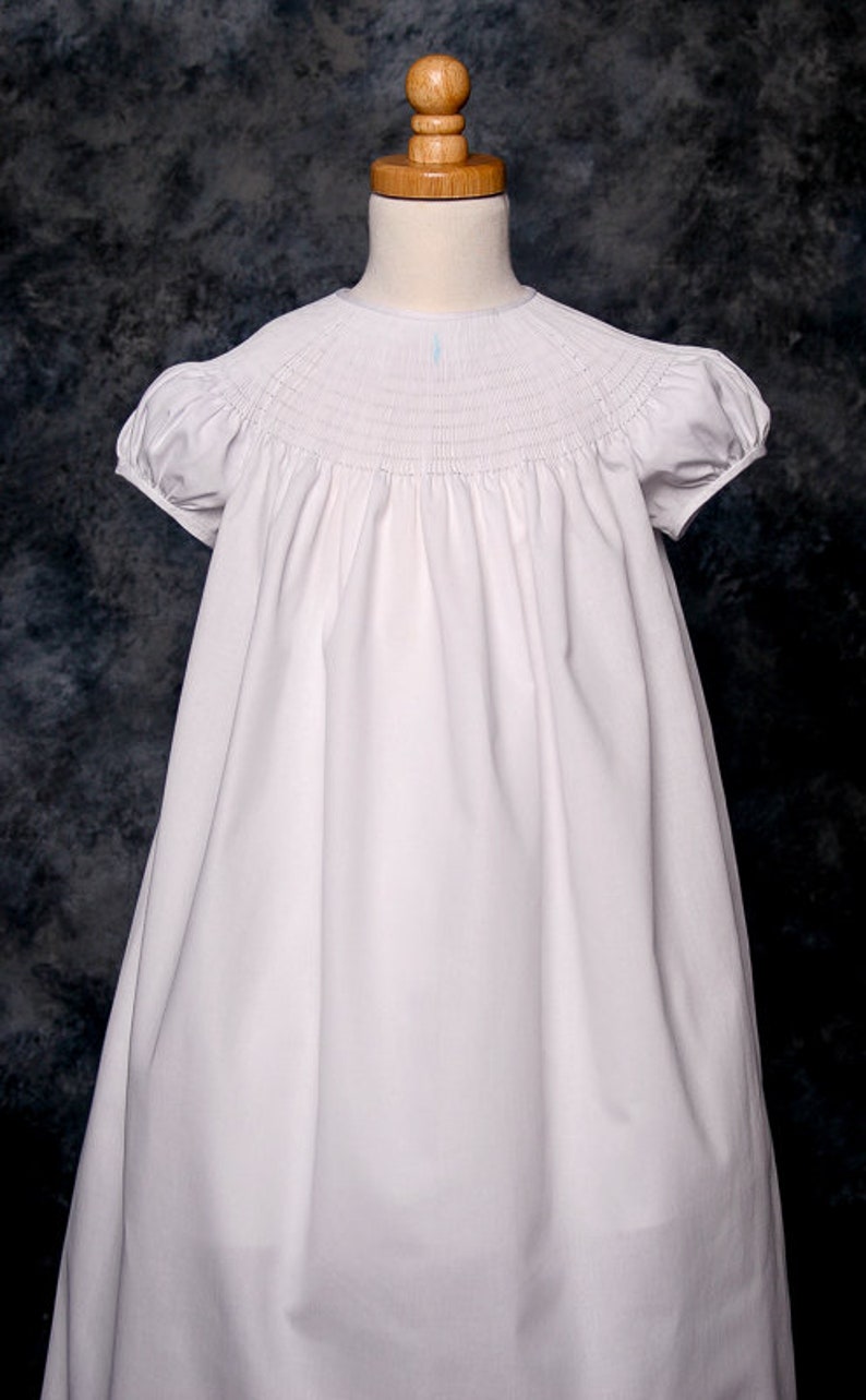 May include: A white smocked dress with short puffed sleeves. The dress is made of a soft, lightweight fabric and has a simple, elegant design.