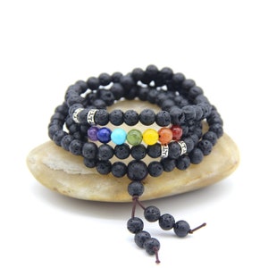 Puede incluir: Un brazalete mala de piedra de lava negra con siete cuentas de chakra. Las cuentas son de los colores del arcoíris, comenzando por el rojo y terminando con el violeta. El brazalete está envuelto alrededor de una piedra marrón claro.