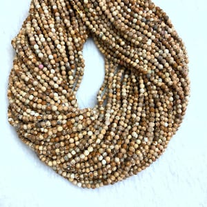 Pode incluir: Um fio de contas de pedras preciosas marrons e brancas. As contas são pequenas e redondas, e têm um aspecto salpicado. As contas são enfiadas em um fio transparente.
