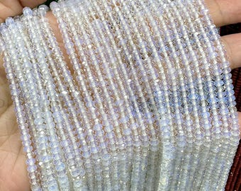May include: Multiple strands of iridescent, round, white beads. The beads have a subtle, shimmering quality, with hints of blue and purple. The beads are held in a hand, showcasing their delicate nature. The beads are likely for jewelry making.