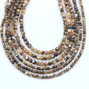 Könnte beinhalten: Mehrere Stränge aus braunen und beigefarbenen, schillernden Muschelkugeln in verschiedenen Größen. Die Perlen haben ein natürliches, organisches Aussehen und sind aufgereiht, wodurch ein geschichteter Effekt entsteht. Auf weißem Hintergrund.