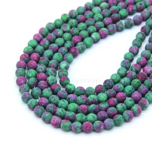 May include: A strand of green and pink gemstone beads. The beads are round and have a speckled appearance.