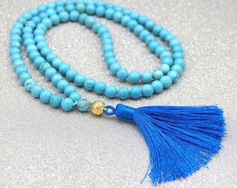 May include: A turquoise blue mala bead necklace with a gold bead and a blue tassel. The necklace is made of round beads and is approximately 108 beads long.