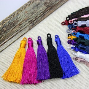 May include: Six colorful silk tassels with a fringe design. The tassels are in the colors yellow, pink, purple, black, and blue.