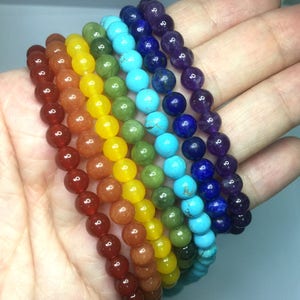 May include: Seven chakra bracelets made of natural stones in the colors of the rainbow. The bracelets are stacked on top of each other, starting with red, orange, yellow, green, blue, indigo, and violet.
