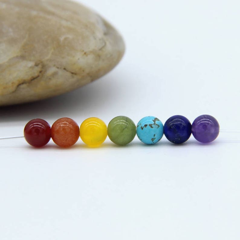 May include: Seven round gemstone beads in the colors of the rainbow chakra system. The beads are red, orange, yellow, green, blue, indigo, and violet.