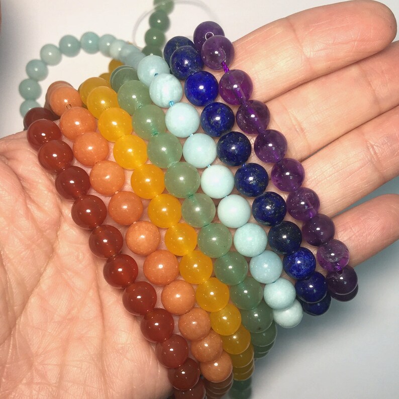 May include: Seven chakra bracelets made of natural stones in a rainbow color pattern. The bracelets are stacked on top of each other, starting with red, orange, yellow, green, blue, indigo, and violet.