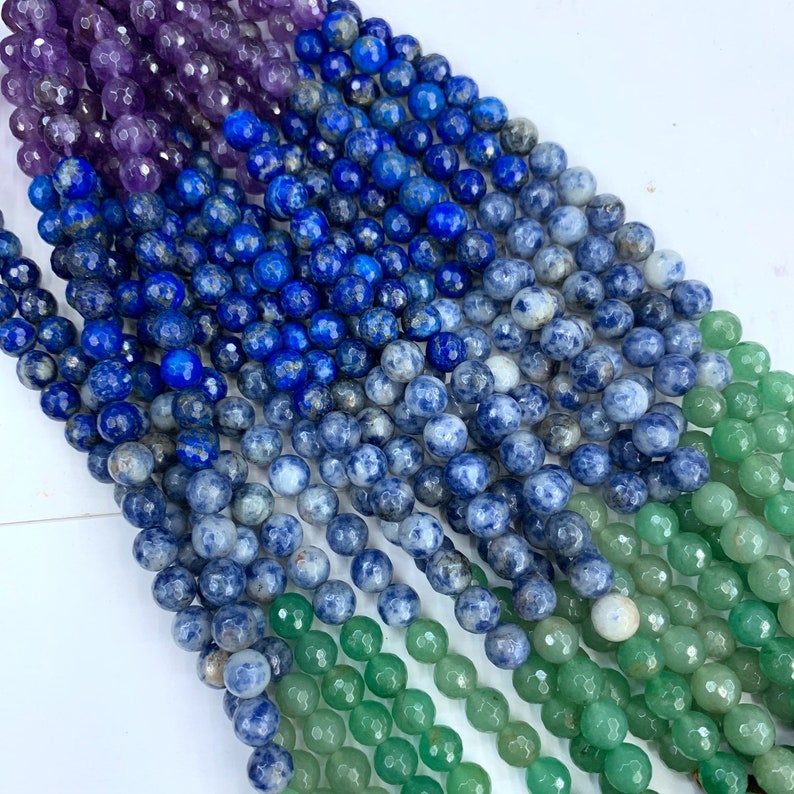 May include: A strand of faceted gemstone beads in shades of purple, blue, and green. The beads are round and have a smooth, polished finish.