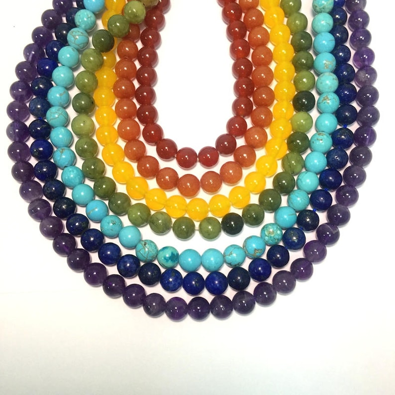 May include: A set of seven chakra gemstone beads in a rainbow color pattern. The beads are arranged in a circle, with the purple amethyst beads at the bottom, followed by blue lapis lazuli, turquoise, green aventurine, yellow citrine, orange carnelian, and red jasper beads.
