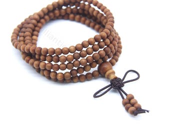 Puede incluir: Una pulsera de cuentas de oración de madera con múltiples hilos de pequeñas cuentas redondas marrones. La pulsera tiene una cuenta decorativa de madera y una borla anudada marrón oscuro. Las cuentas están ensartadas, creando un efecto en capas.