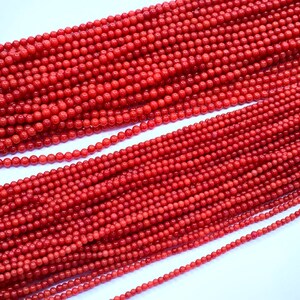 May include: Strands of small, round, bright red beads. The beads are uniform in size and appear to be strung together, creating a textured surface. The beads are closely packed together, filling the frame.