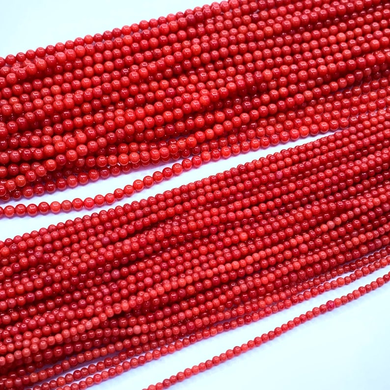 May include: Strands of small, round, bright red beads. The beads are uniform in size and appear to be strung together, creating a textured surface. The beads are closely packed together, filling the frame.