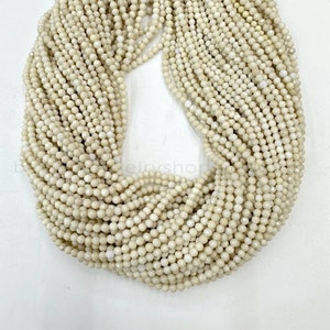 以下が含まれることがあります： オフホワイトのファセットカットされた宝石ビーズのストランド。ビーズは小さく丸く、透明な糸に糸でつながれています。ビーズは円形に配置されており、すべて同じサイズと形です。