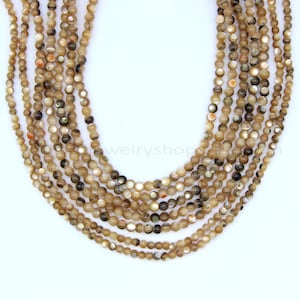 May include: Multiple strands of small, round, beige beads with iridescent and dark brown highlights. The beads are of varying sizes and strung together. These beads are likely for jewellery making.
