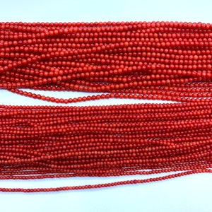 May include: Close-up of multiple strands of red coral beads. The beads vary in size, with the largest at the top and the smallest at the bottom. The beads are a vibrant, uniform red color, and are strung together, creating a textured surface.