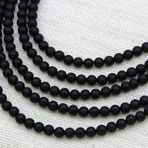 May include: A strand of black matte round beads. The beads are strung on a clear thread and are arranged in a circular pattern.