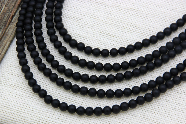 May include: A strand of black matte round beads. The beads are strung on a clear thread and are arranged in a circular pattern.