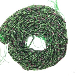 Può includere: Un filo di perline di pietre preziose verdi e rosa. Le perline sono sfaccettate e hanno una forma leggermente irregolare. Le perline sono infilate su un filo sottile.
