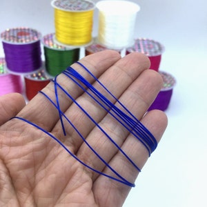 Puede incluir: Primer plano de una mano sosteniendo un carrete de cord&oacute;n el&aacute;stico azul. El cord&oacute;n es delgado y flexible, y es perfecto para hacer joyas u otras manualidades.