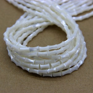 May include: A strand of white, iridescent, shell beads in a bamboo shape. The beads are strung together and are approximately 10mm in diameter.
