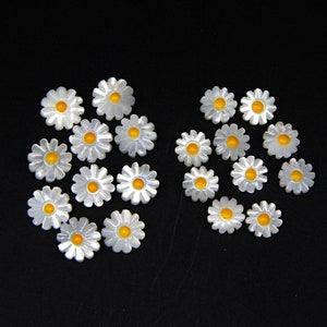 May include: A collection of white daisy-shaped buttons with yellow centers. The buttons are arranged in two groups, one larger than the other.