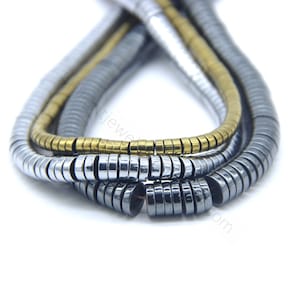 Könnte beinhalten: Drei Stränge Perlen, eine gold, eine silber und eine schwarz, sind in einem Kreis angeordnet. Die Perlen sind alle rund und haben eine leicht abgeflachte Form.
