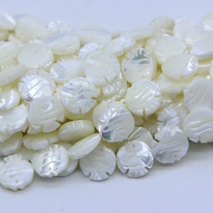 Może przedstawiać: Stos białych pereł z masy perłowej z wygrawerowanym wzorem ryby na każdej perle.