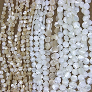 Op de afbeelding: Een close-up van meerdere strengen ronde schelpparels in wit en crème. De parels zijn glad en hebben een lichte iriserende glans.