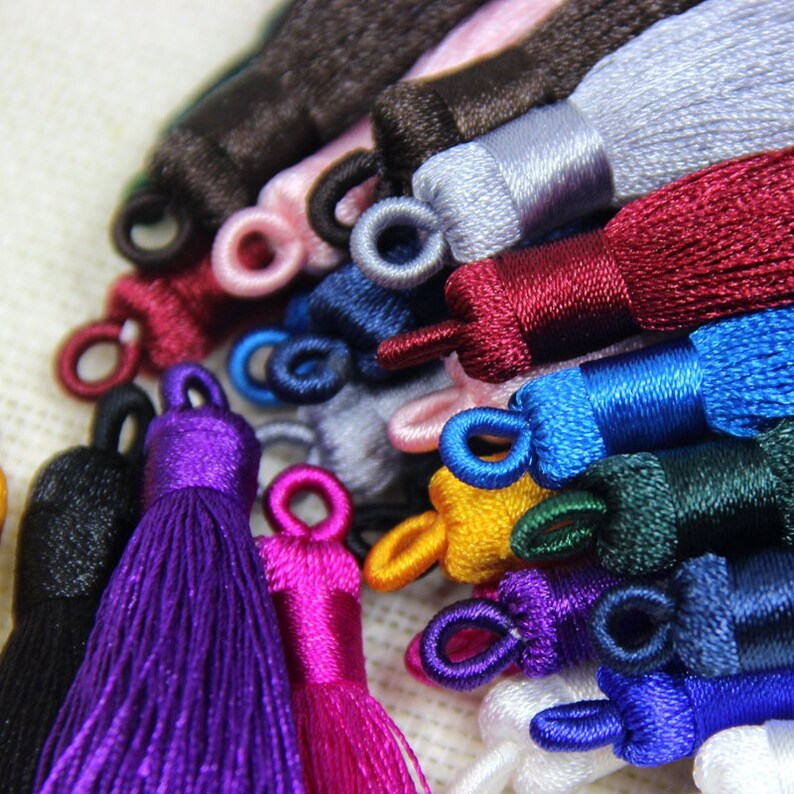 May include: Assortment of colorful tassel trims in various colors, including black, purple, pink, blue, green, yellow, and white. The tassels are made of soft, silky fabric and have a loop at the top for easy attachment.