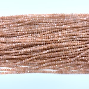 Könnte beinhalten: Eine Strähne aus pfirsichfarbenen Sunstone-Perlen. Die Perlen sind facettiert und haben eine quadratische Form. Die Perlen sind auf einem durchsichtigen Faden aufgefädelt.