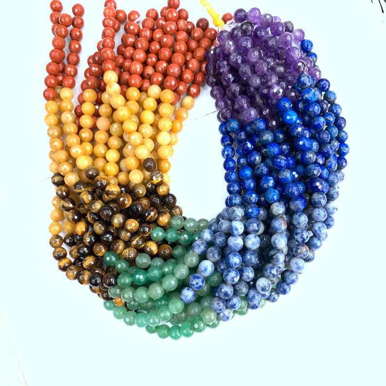 May include: A rainbow of gemstone beads, including red, orange, yellow, green, blue, and purple. The beads are round and have a smooth, polished finish.