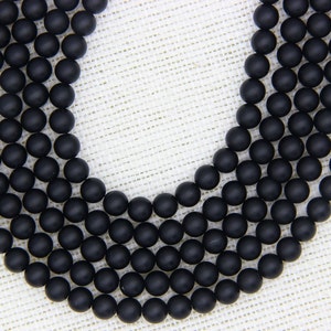 May include: A strand of black matte round beads. The beads are arranged in a circular pattern, with the ends of the strand overlapping.