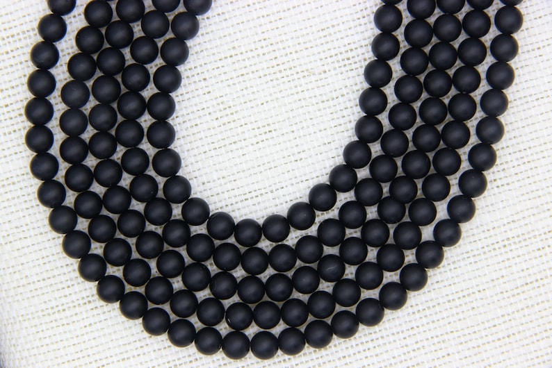 May include: A strand of black matte round beads. The beads are arranged in a circular pattern, with the ends of the strand overlapping.