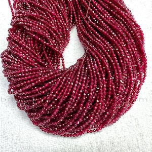 Peut inclure: Un grand ensemble de perles rouge foncé à facettes. Les perles sont enfilées ensemble, créant un aspect dense et texturé. La couleur est un rouge foncé riche, avec un léger éclat des facettes. Les perles sont probablement destinées à la fabrication de bijoux.