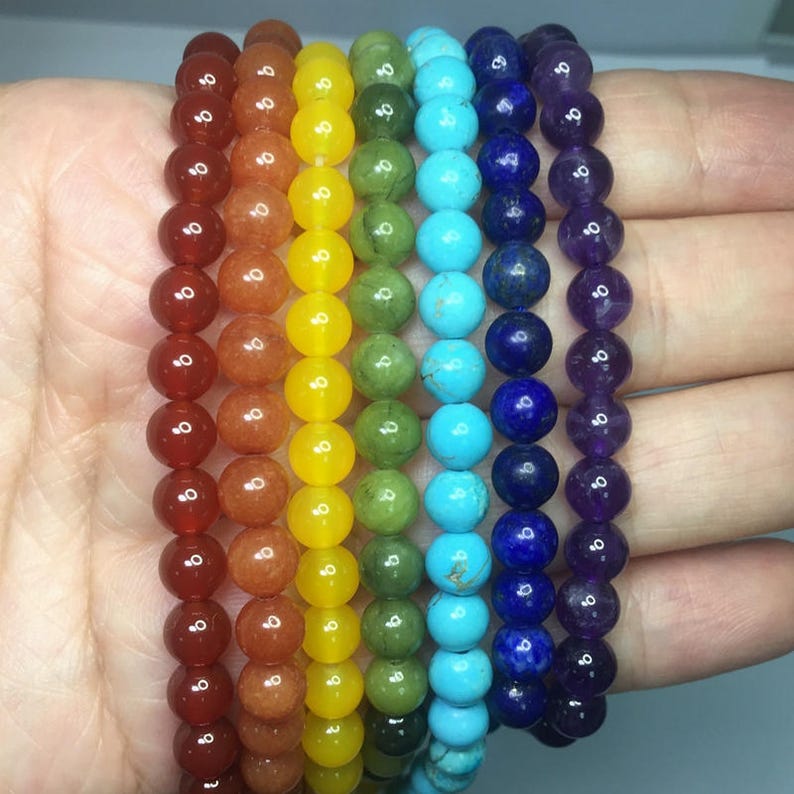 May include: Seven colorful beaded bracelets stacked on top of each other. The bracelets are red, orange, yellow, green, blue, turquoise, and purple.