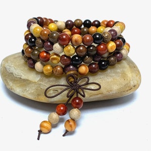 Op de afbeelding: Een veelkleurige houten kralen armband met een bruine kwast. De armband is gemaakt van verschillende soorten hout, waaronder sandelhout, rozenhout en ebbenhout. De kralen zijn allemaal van verschillende grootte en vorm, en de armband is zeer ingewikkeld.